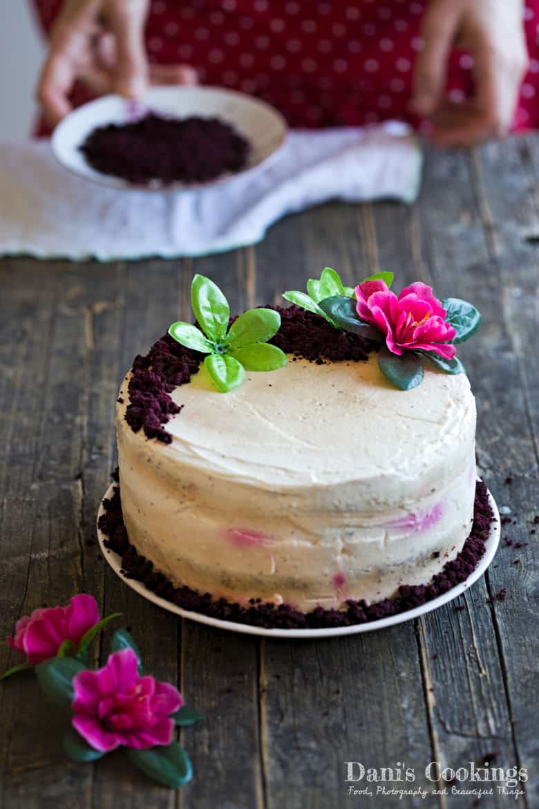 a cake with white frosting and flowers and a woman behind