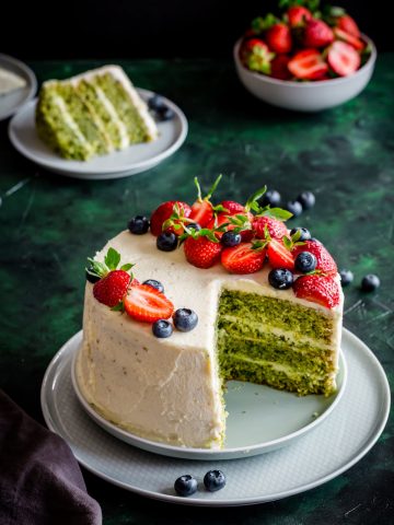 a cake with green layers and white frosting and berries, cut
