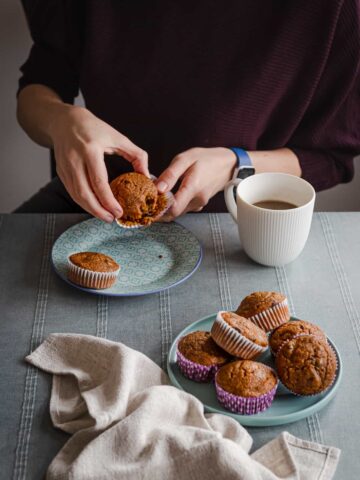 a woman eating muffin on a table with more aside