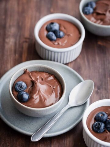 four ramekins of chocolate mousse decorated with blueberries