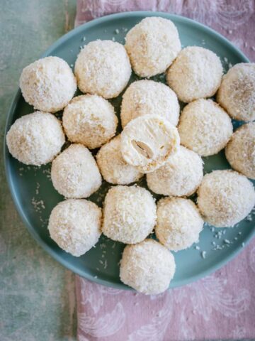 White coconut balls on a plate one cut in half with almond inside