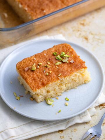 a slice of revani in a plate in front of the pan with the cale